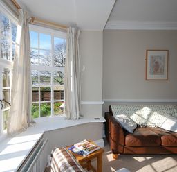 A living room with a brown leather sofa near a large bay window with curtains at Beach House Alnmouth
