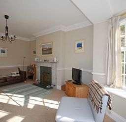 A living room with a sofa a fireplace a television and a window with curtains at Beach House (Alnmouth) in Alnmouth