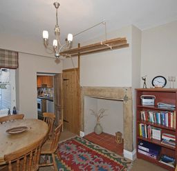 A dining room with a wooden table and chairs a bookshelf a fireplace and a window with a beach sign at Beach House (Alnmouth) in Alnmouth