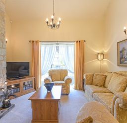 A living room with a stone fireplace a television on a wooden cabinet an armchair a sofa a coffee table and a large window with curtains at Lavender Cottage Village Farm in Seahouses