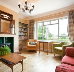 A living room with a green armchair a red sofa and a wooden table with a plant at Estuary View in Alnmouth