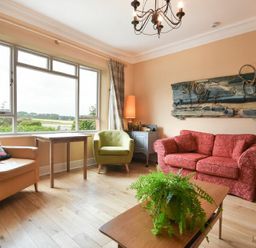 A living room with a red sofa green and beige armchairs a wooden coffee table with a plant and a decorative wall piece at Estuary View in Alnmouth