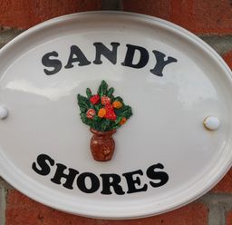 An oval white plaque with the words sandy shores and a flower vase mounted on a brick wall