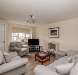 A living room with grey sofas a TV on a stand a small glass coffee table and a fireplace at Sandy Shores in Seahouses