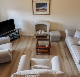 A living room with beige sofas a glass coffee table a television on a stand a decorative fireplace and a floor lamp at Sandy Shores in Seahouses