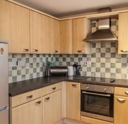 A kitchen with wooden cabinets a stainless steel oven a stovetop a silver refrigerator and a tiled backsplash at Sandy Shores in Seahouses