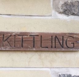 A wooden sign with the word Kittling carved into it mounted on a stone wall at Kittling Cottage in Bamburgh