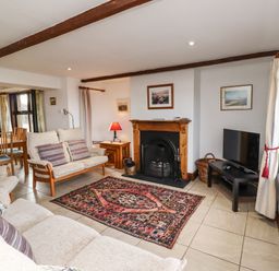 A living room with sofas a rug a fireplace a television and a dining area at Kittling Cottage in Bamburgh