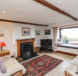 A living room with sofas a fireplace a television and a window seat at Kittling Cottage in Bamburgh