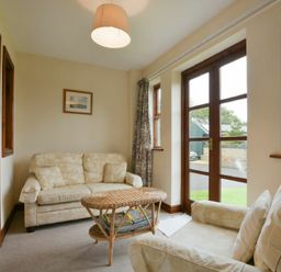 A sitting room with two sofas a wicker coffee table and glass doors at Smithy Court in Craster