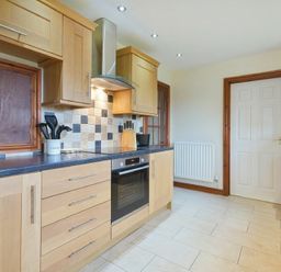 A kitchen with wooden cabinets a built in oven and a closed white door at Smithy Court in Craster