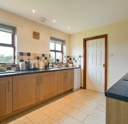 A kitchen with wooden cabinets black countertops tiled floor and a white door at Smithy Court in Craster