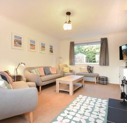 A living room with two sofas an armchair a coffee table a fireplace and a window with curtains at Barmoor in Embleton