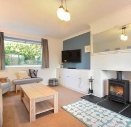 A living room with a sofa, armchair, coffee table, fireplace, television, and a window at Barmoor in Embleton