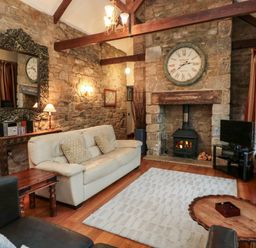 A living room with a stone fireplace a clock above and a cream sofa at Lapwing Cottage in Bamburgh