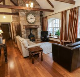 A living room with two sofas a stone fireplace and large windows with curtains at Lapwing Cottage in Bamburgh