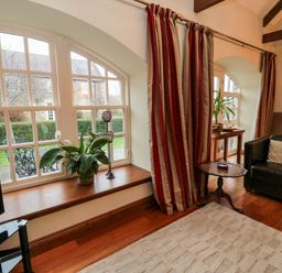 A living room with arched windows with plants on the windowsill a black leather sofa a wooden side table and striped curtains at Lapwing Cottage in Bamburgh