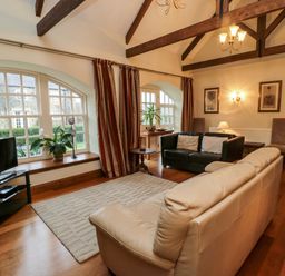 A living room with two sofas a television large windows and exposed ceiling beams at Lapwing Cottage in Bamburgh