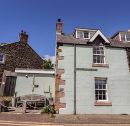 A house with a bench and sign on Dunstanburgh Road at Marie's Cottage in Craster