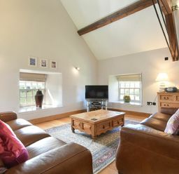 A living room with two leather sofas a wooden coffee table a TV and wooden beams at Budle Sands in Bamburgh