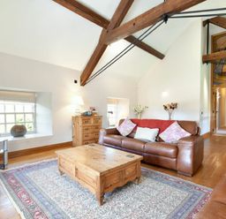 A living room with leather sofas wooden coffee table wooden chest of drawers and exposed ceiling beams at Budle Sands in Bamburgh