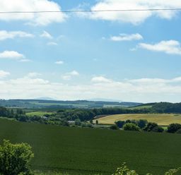 A landscape with fields trees and hills under a blue sky at Budle Sands Bamburgh