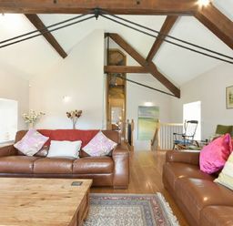 A living room with brown leather sofas wooden coffee table exposed wooden beams and a rug at Budle Sands in Bamburgh