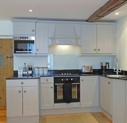 A kitchen with white cabinets black countertops a stove toaster and wooden door at Dorothy Forster Court in Alnwick