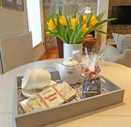 A dining table with a tray containing a teapot cups shortbread fingers and a wrapped gift with yellow flowers in a vase in the background at Dorothy Forster Court in Alnwick
