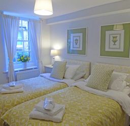A bedroom with two single beds yellow patterned bedding pillows and towels beside a window at Dorothy Forster Court in Alnwick