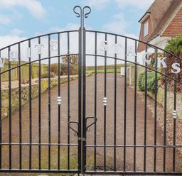 A black metal gate with the words White Stacks at the entrance to a property with stone walls and a driveway at Whitestacks in Bamburgh