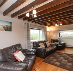 A living room with three black leather sofas a window with curtains and a floor lamp at Whitestacks in Bamburgh