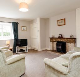 A sitting room with two armchairs a television on a stand a fireplace with a clock and framed pictures on the walls at Bilton Farm Cottage No1 in Alnmouth