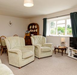 A living room with armchairs a television on a stand a side table with a lamp and a dining table with chairs at Bilton Farm Cottage No1 in Alnmouth