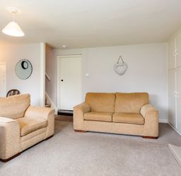 A living room with two beige sofas a fireplace built in cupboards a wall clock and a heart decoration at Bilton Farm Cottage No2 in Alnmouth
