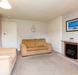 A living room with two beige sofas a fireplace and a framed beach picture at Bilton Farm Cottage No2 Alnmouth