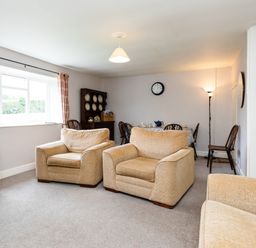 A living room with two beige armchairs a dining table with chairs a wooden cabinet and a staircase at Bilton Farm Cottage No2 in Alnmouth