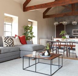 A living room with a gray sectional sofa and a wood and metal coffee table near a dining area with a wooden table and chairs under exposed wooden beams at Lantern View Eglingham