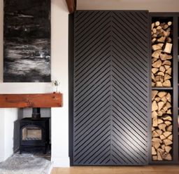 A fireplace with a wood-burning stove and a wooden mantel next to a shelf with firewood and decorative items at Lantern View in Eglingham