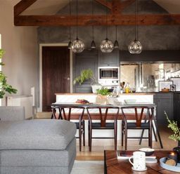 An open plan living room and kitchen with wooden beams wooden dining chairs and a gray sofa at Lantern View in Eglingham