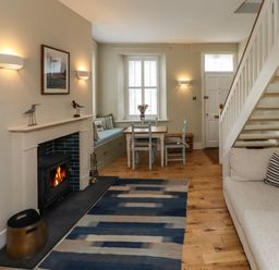 A living room with a fireplace a sofa stairs and a dining table at Strandline in Alnmouth