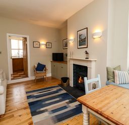 A living room with a fireplace a wooden table sofa armchair and a blue rug at Strandline Alnmouth