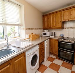 A kitchen with wooden cabinets a washing machine a microwave and a stove at Strandline Alnmouth