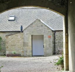 A stone building with a white door seen through a stone archway at Swallow Cottage nr Powburn in Powburn