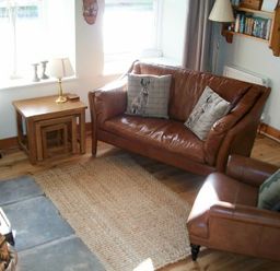 A living room with two leather chairs a wooden side table with a lamp and a woven rug at Swallow Cottage nr Powburn in Powburn