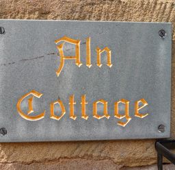 A stone plaque with the text Aln Cottage mounted on a brick wall at Aln Cottage Alnwick