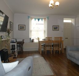 A living room with sofas a dining table wooden chairs a wall-mounted tv a fireplace and a window with bunting at Aln Cottage Alnwick