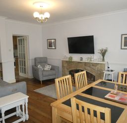 A living room with wooden dining table and chairs a stone fireplace with a mounted TV and gray armchairs at Aln Cottage in Alnwick