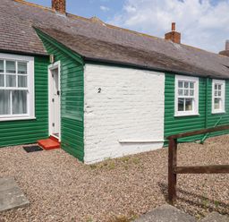 A green and white cottage with multiple windows and a white door on a gravel yard at Armstrong Cottages No2 in Bamburgh