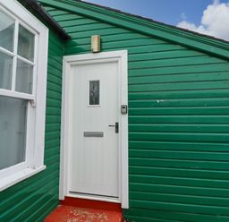 A green exterior wall with a white door and window at Armstrong Cottages No2 in Bamburgh